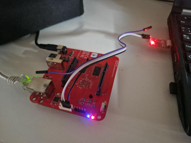 Odroid HC4 single-board computer laying on a desk. Connected to power, ethernet
and via an USB UART adapter to a laptop. The blue "alive" LED is lit - it has
successfully booted into Linux!