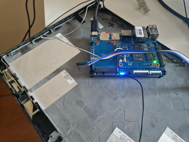 The blue Banana Pi board sitting inside a laptop lid backplate, gray and black antena cables from the lid are connected to its antena connectors. The ethernet cable is unplugged.