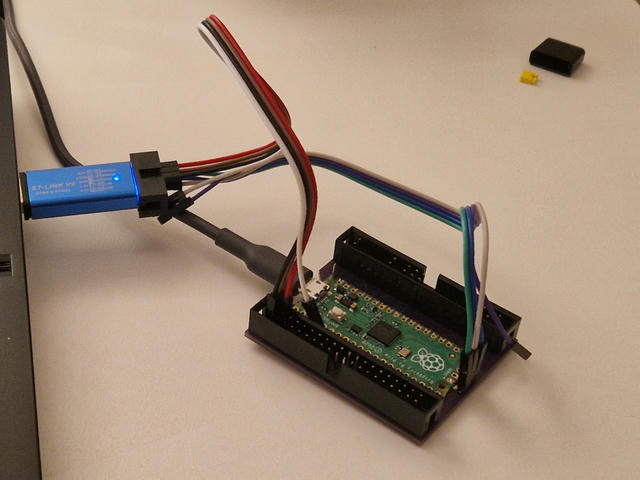 STLink debugger plugged in into a laptop. It looks like a shiny blue USB
drive with a blue LED except it has a 10 pin header connector at the end. It's
connected to a Raspberry Pi Pico board with two sets of 4 wire jumpers, each has
one wire unused, one is connected to the Pico SWD header and one is connected at
the opposite side of the board where the UART pins are.